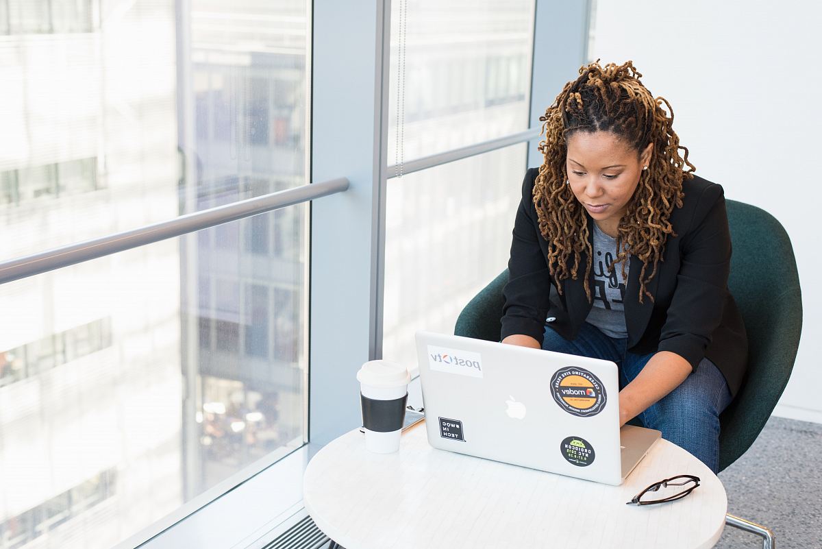 woman sits on padded chair while using MacBook during daytime